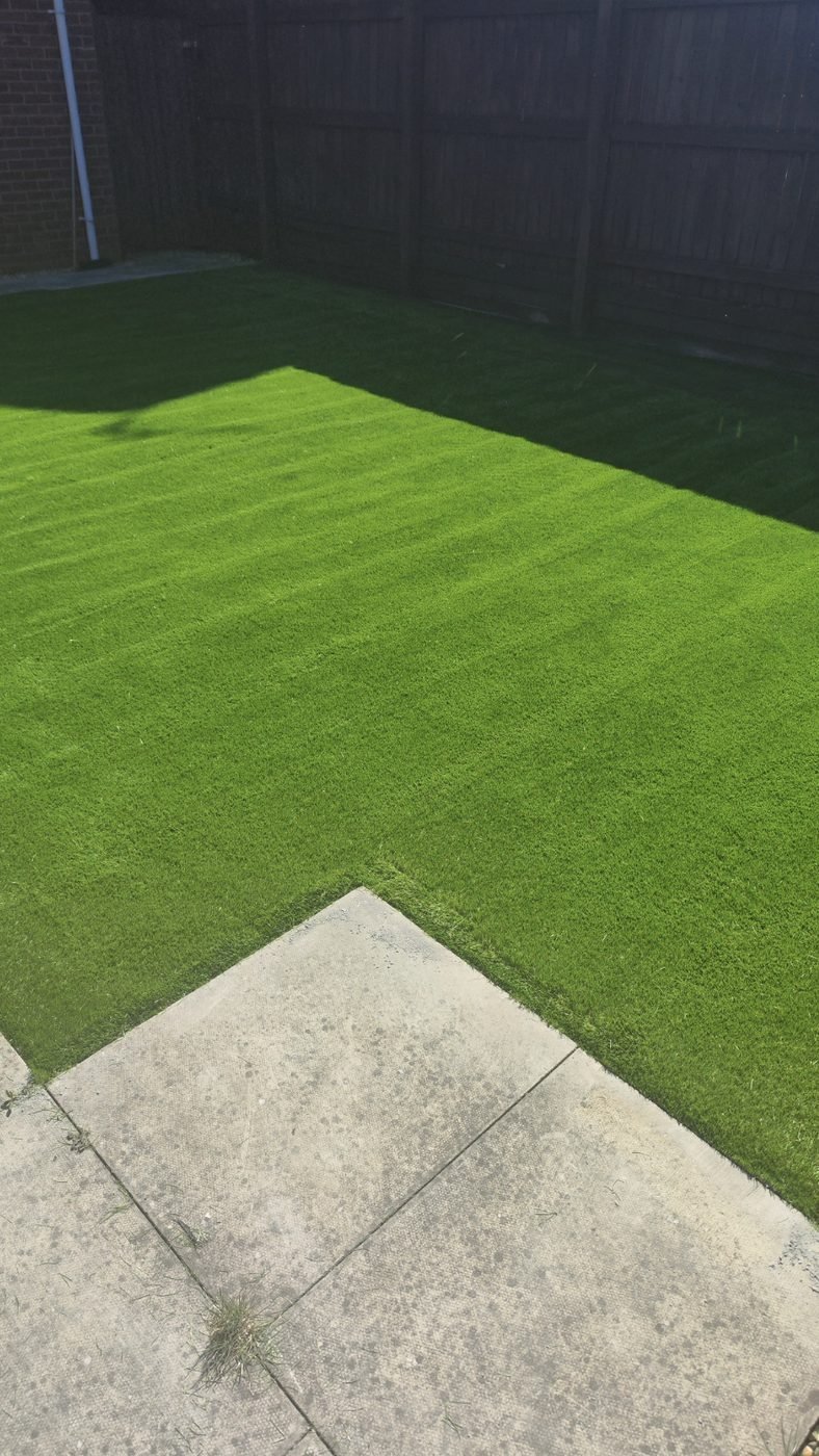 Close view of a dark green artificial grass lawn meeting a paved edge in a fenced garden