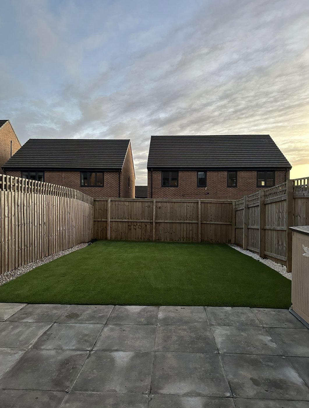 Artificial grass lawn with gravel margins in a new build garden at dusk with a paved patio