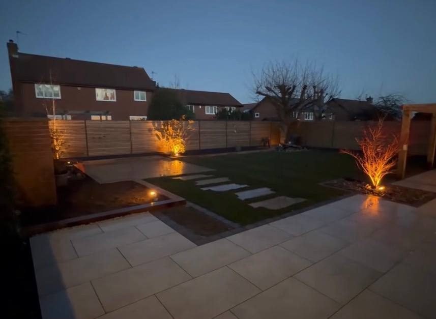 Garden at dusk with uplit trees, lit stepping stones and a paved terrace