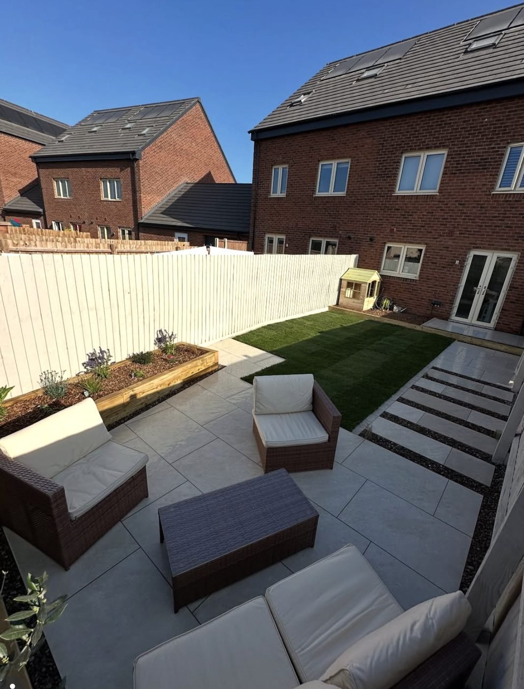 Grey porcelain patio with rattan seating, a sleeper raised bed and stepping stones through the lawn