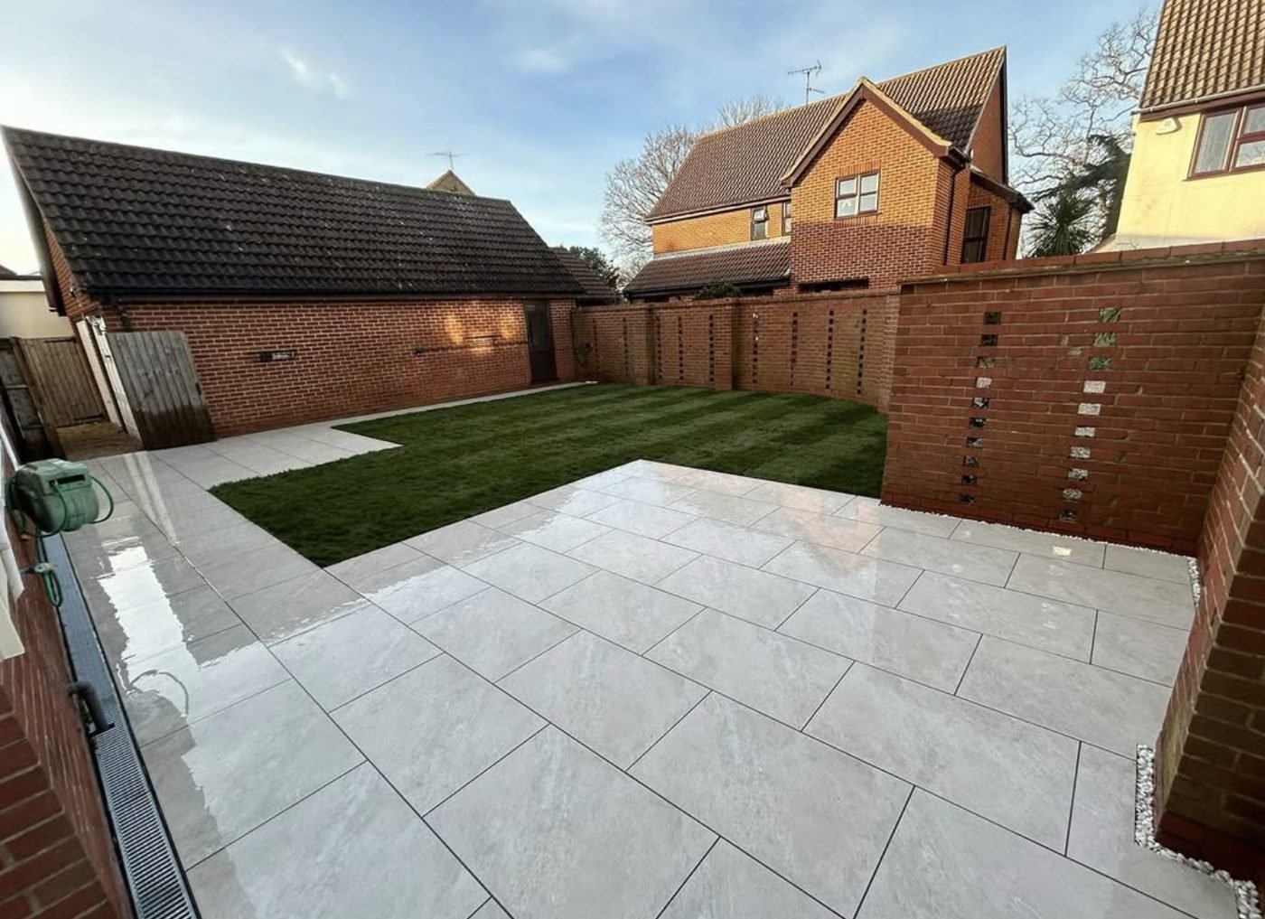 Light porcelain patio with a freshly laid turf lawn behind it enclosed by brick walls