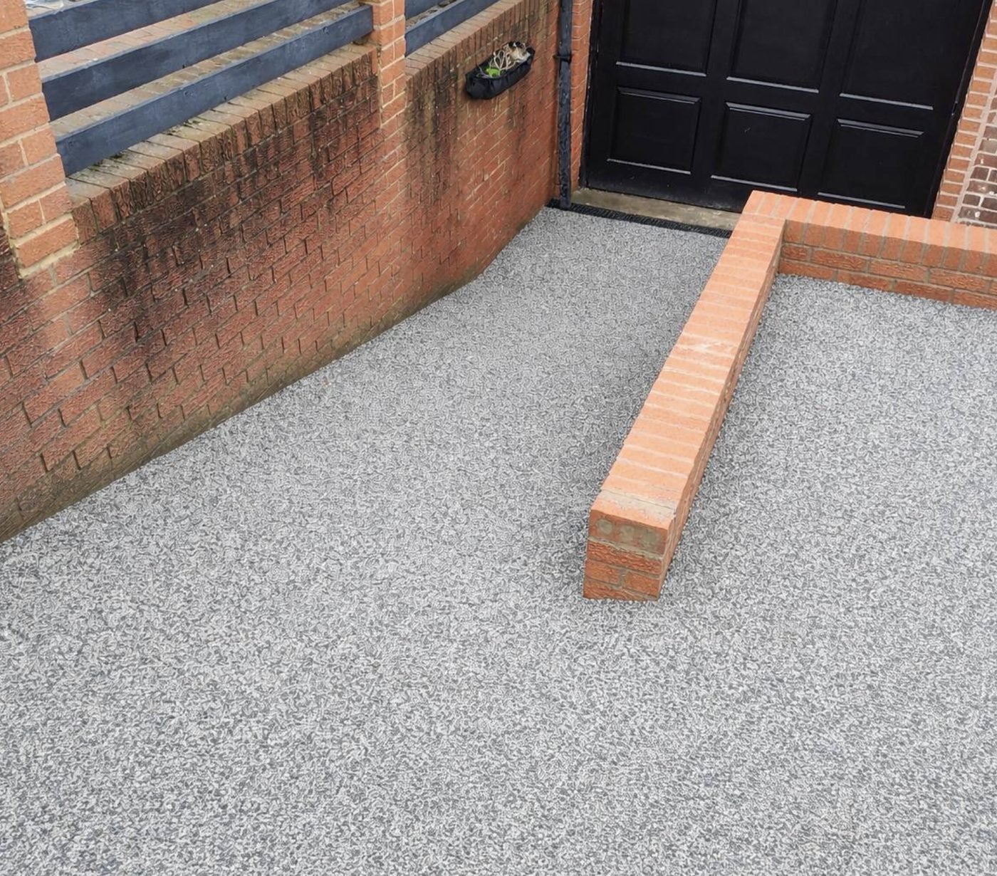 Grey resin bound driveway laid up to a brick wall and black garage doors