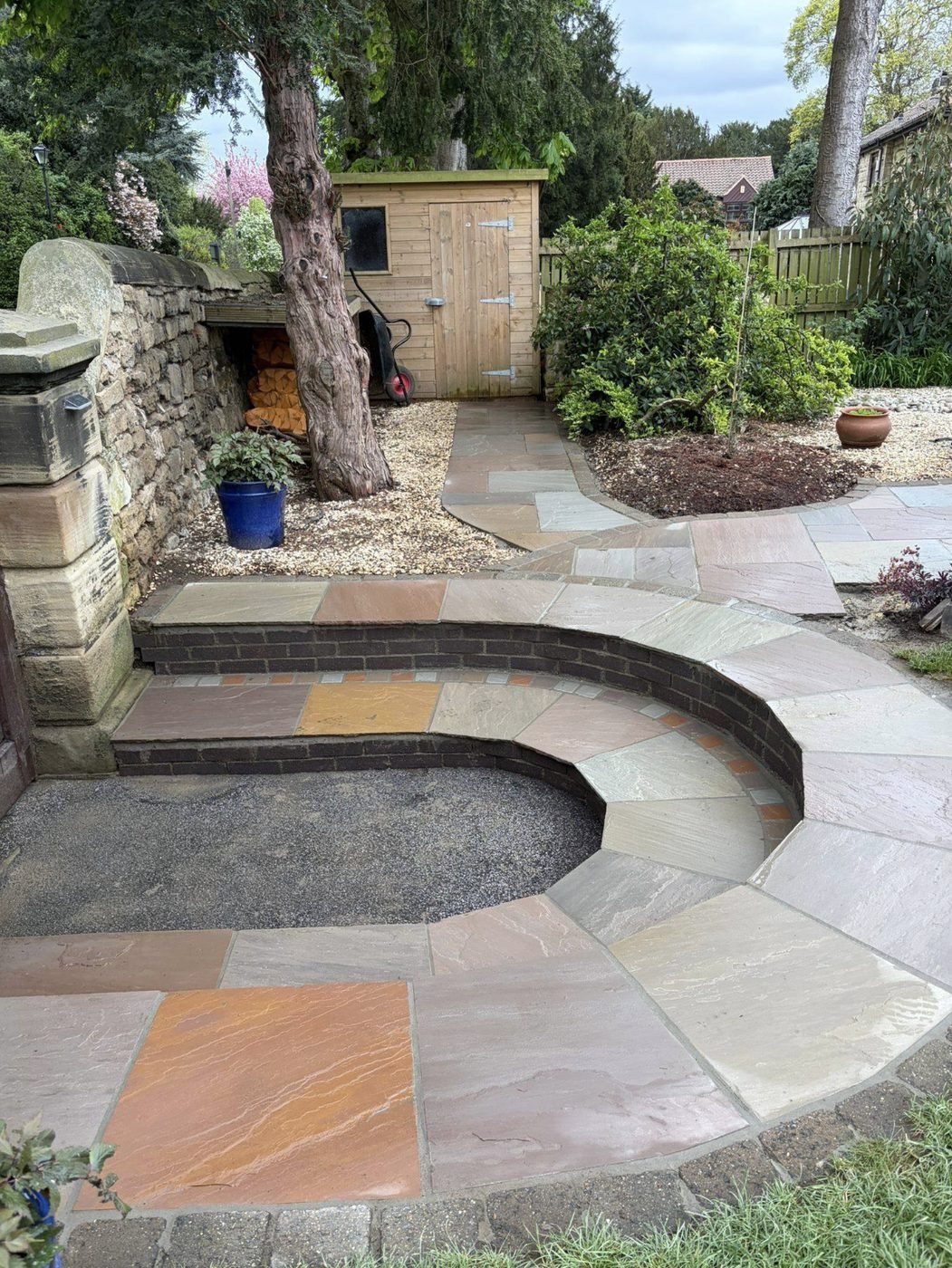 Curved Indian sandstone patio with brick edged radius steps leading to a shed and gravel bed