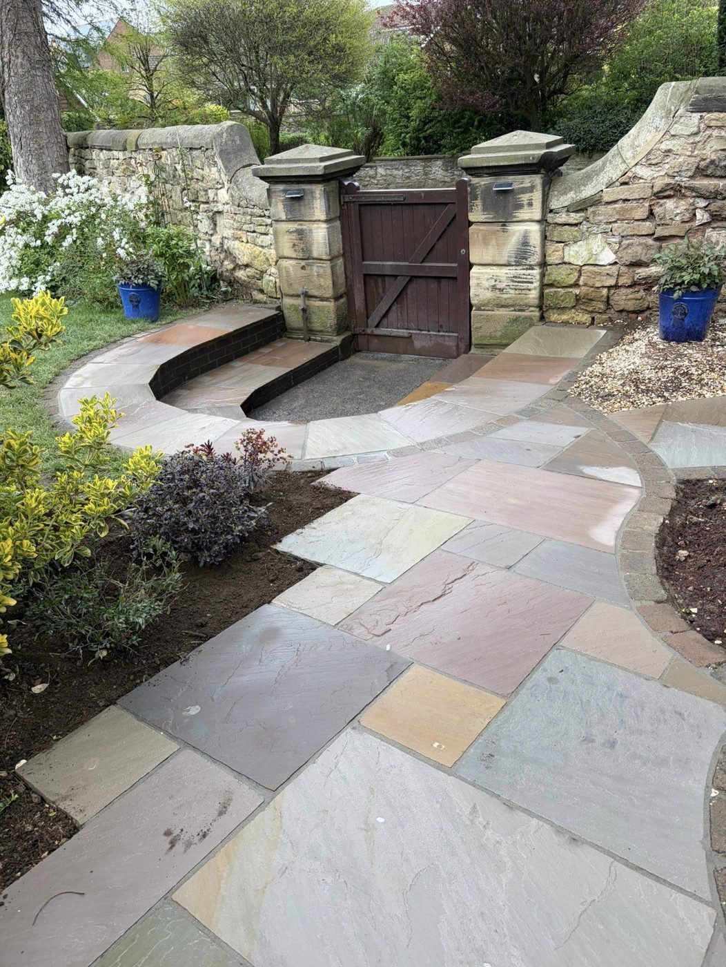 Indian sandstone path curving through a stone walled garden to a timber gate between stone gate posts
