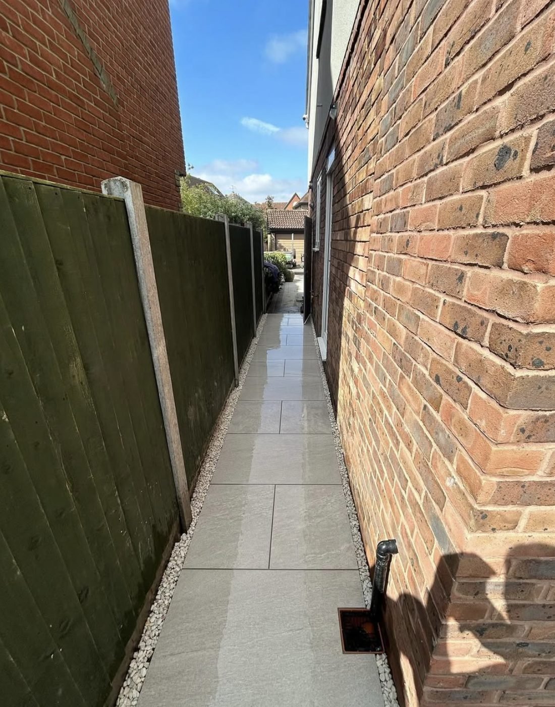 Narrow porcelain side path between a house wall and a fence with white pebble margins